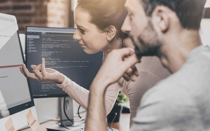 Two persons in front of computer, one explaining to the other